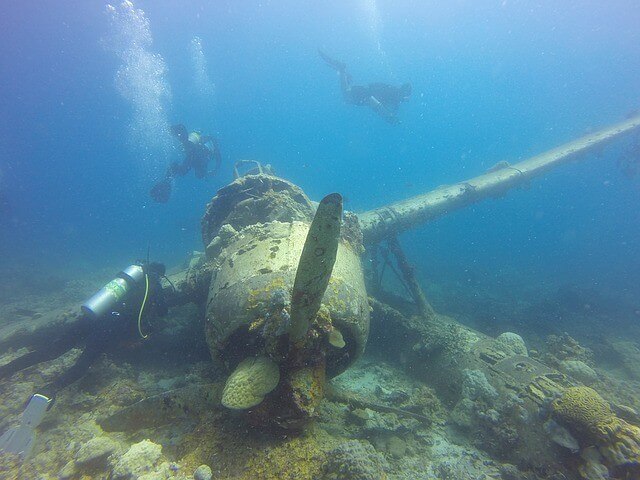Japanese WWII plane wreck on bottom of ocean with three scuba divers