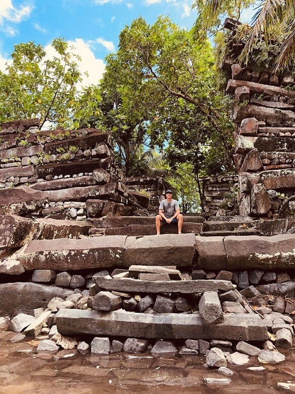 man sitting in nan madol ruins of large stone slabs