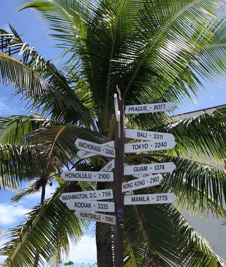 street sign with distances to world cities with palm tree in background