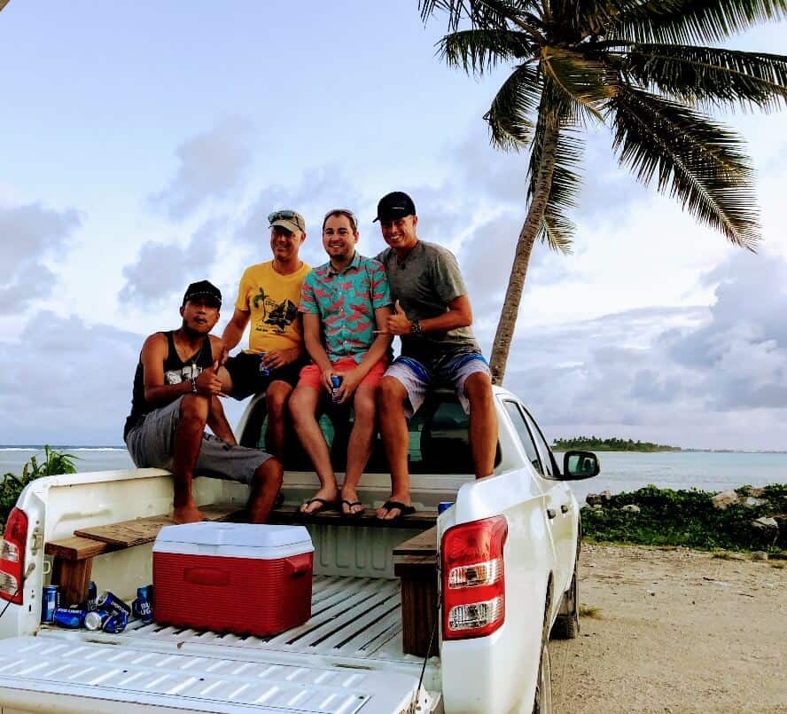 white pickup truck with four men sitting in back with palm tree in background