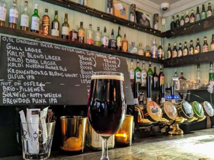 glass of Dark Lager on a bar with bottles in background