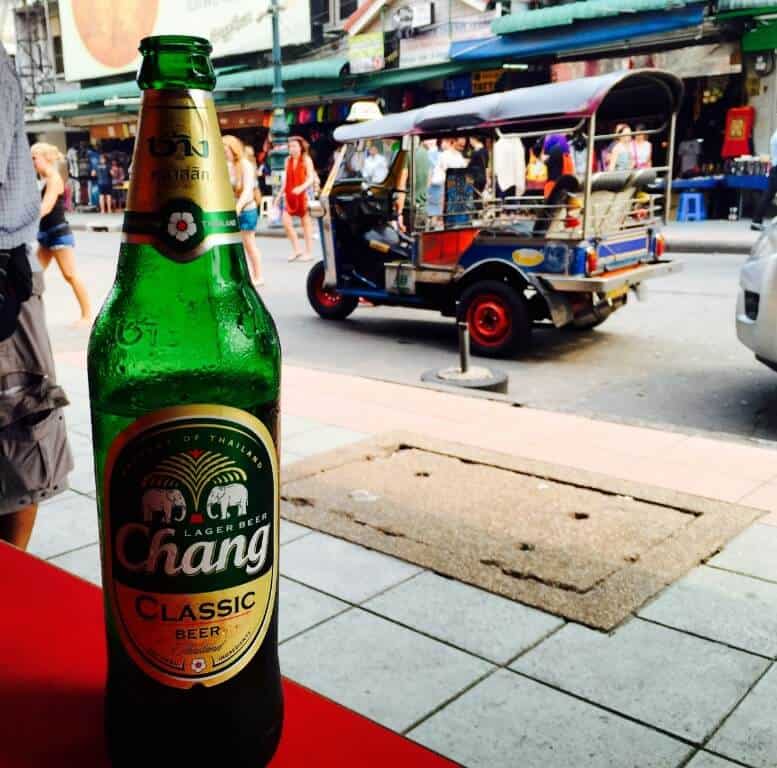 Chang beer bottle on Bangkok street with tuk-tuk next to it.