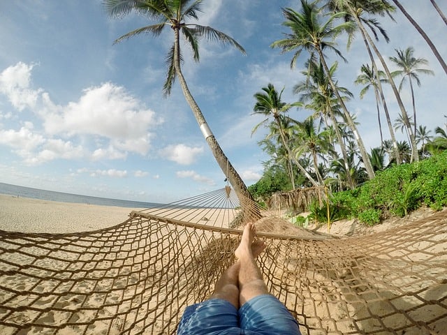 Mann in Hängematte am Strand mit Palmen auf Caye Caulker