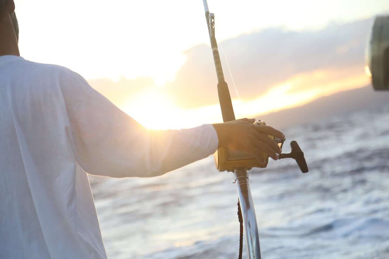 man holding fishing pole at sunset