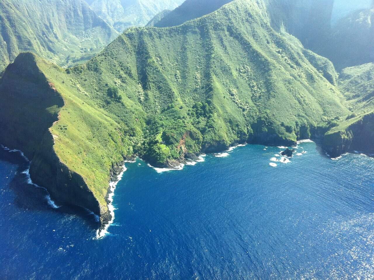 tall green Molokai sea cliffs and ocean seen from air