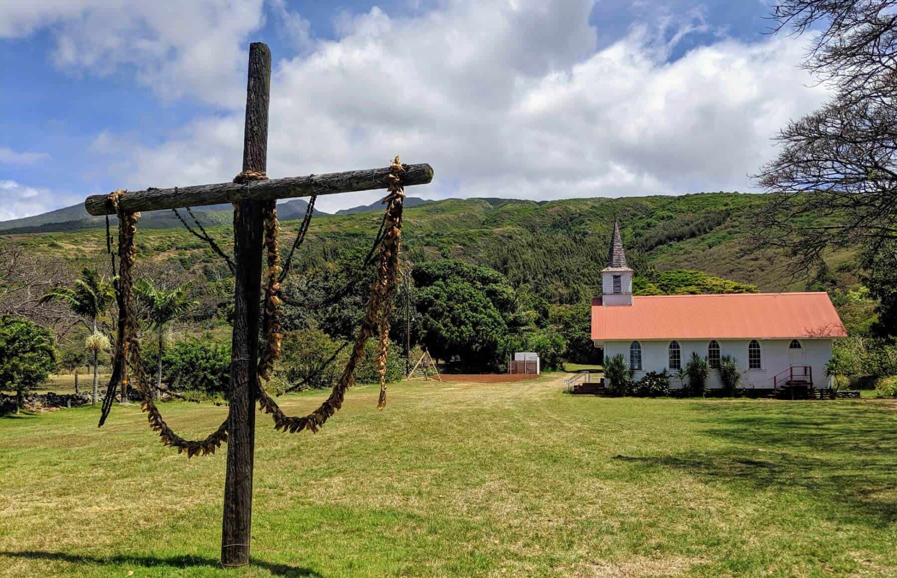 large wooden cross with leis and red and white Church in backgound