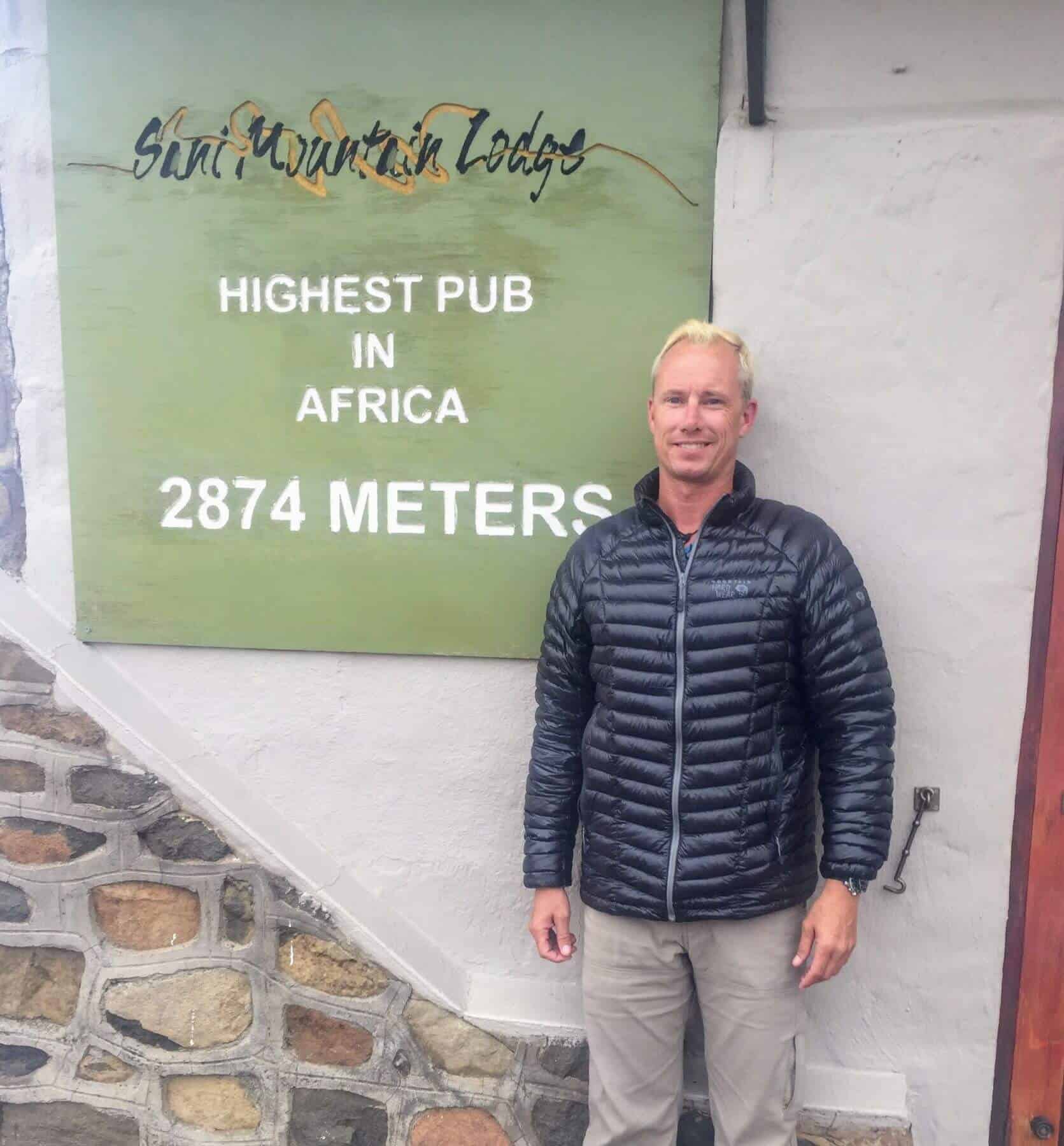 man next to The Highest Pub in Africa sign