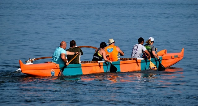 six people on orange and blue outrigger canoe in ocean